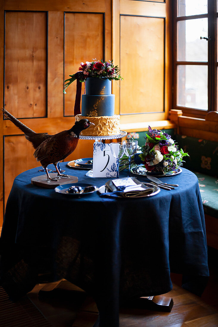 Stuffed pheasant, cake and flowers on table set in blue