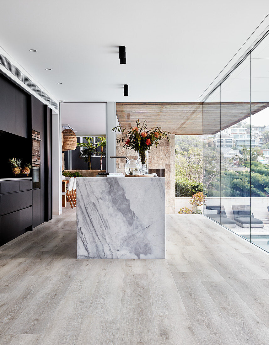 Marble island counter in open-plan kitchen with wooden floor and glass wall