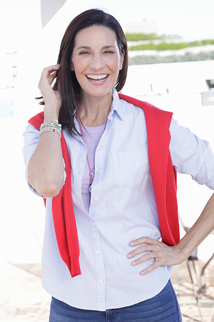 A brunette woman wearing a light shirt with a red jumper over her shoulders