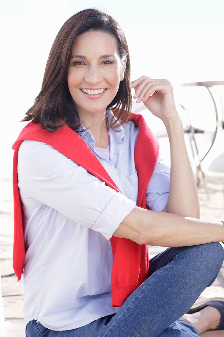 A brunette woman wearing a light shirt with a red jumper over her shoulders