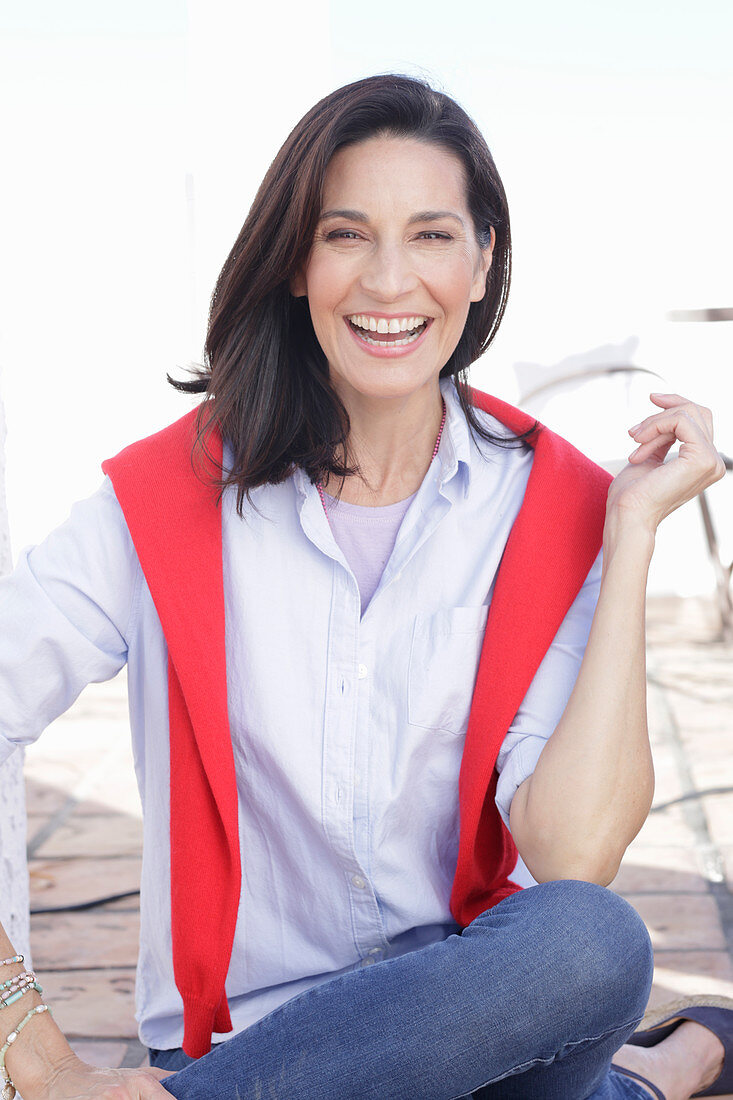 A brunette woman wearing a light shirt with a red jumper over her shoulders