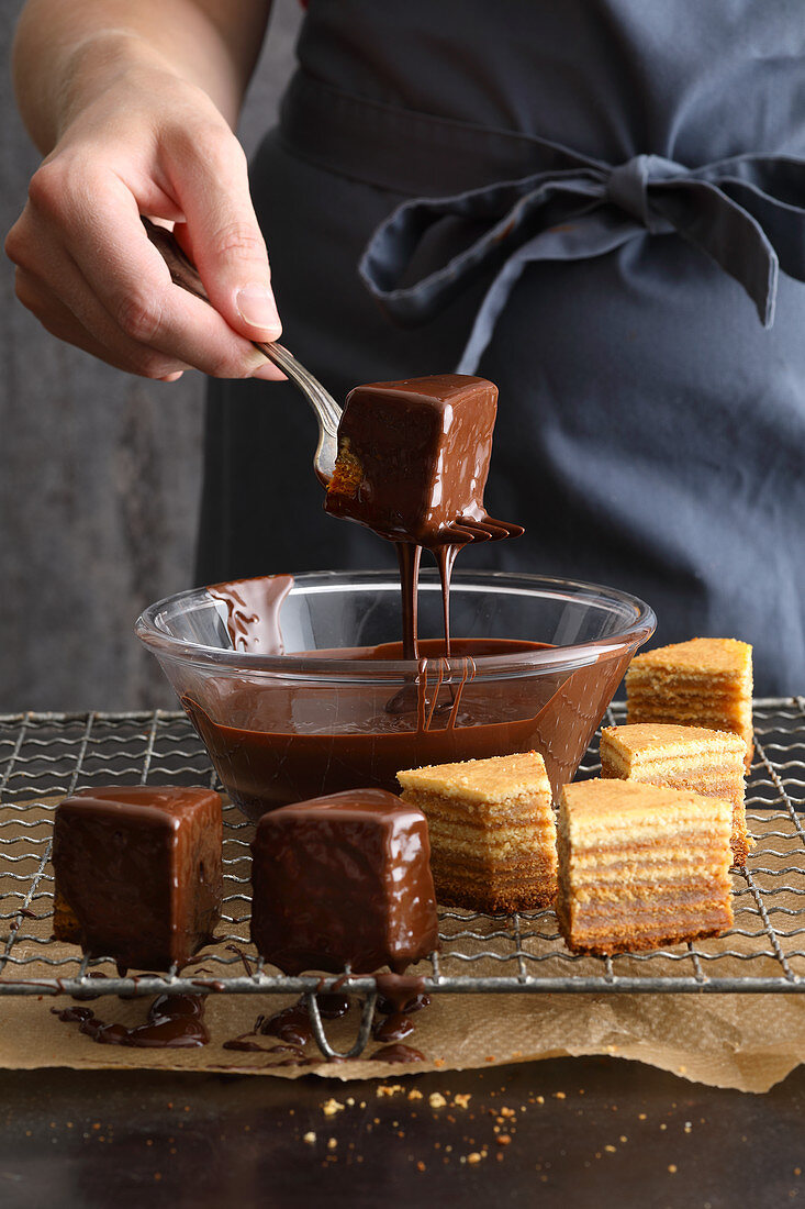 Pieces of Baumkuchen (German layer cake) being dipped into melted chocolate