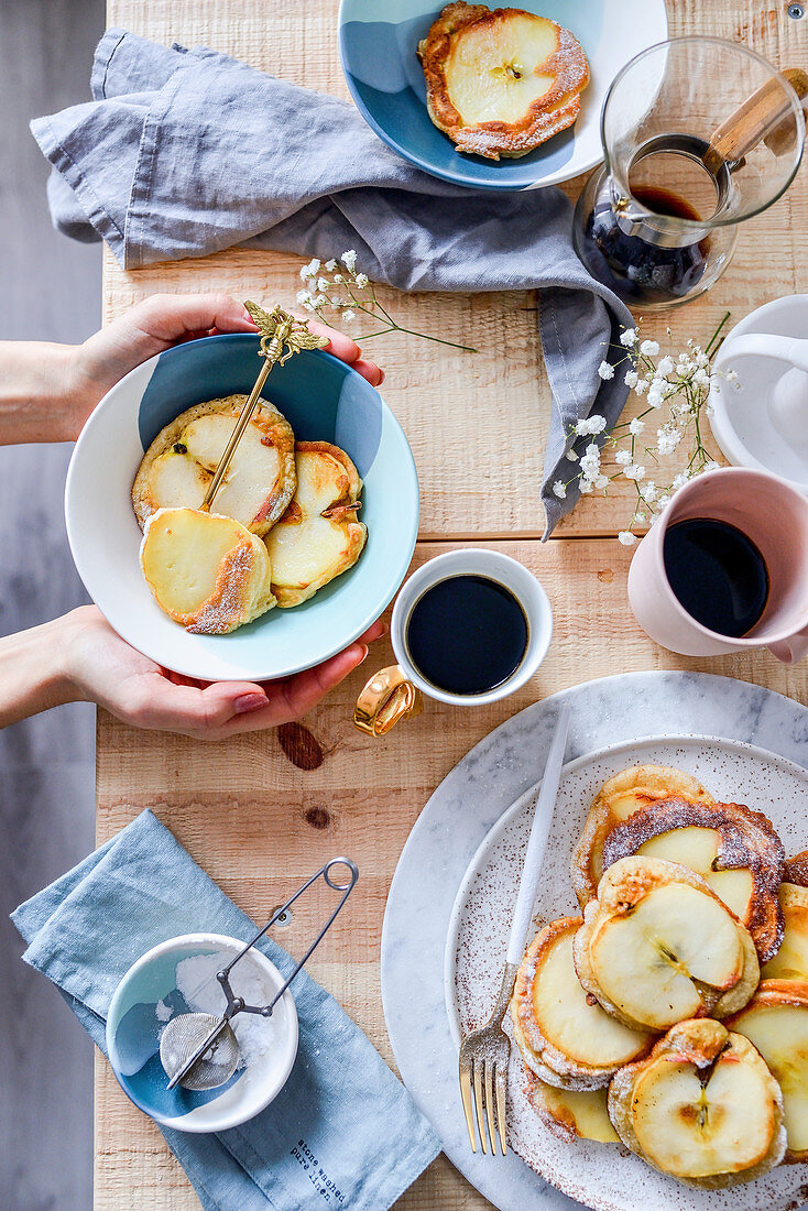Pancakes with apples on the table with breakfast coffee mugs plates with food wooden table