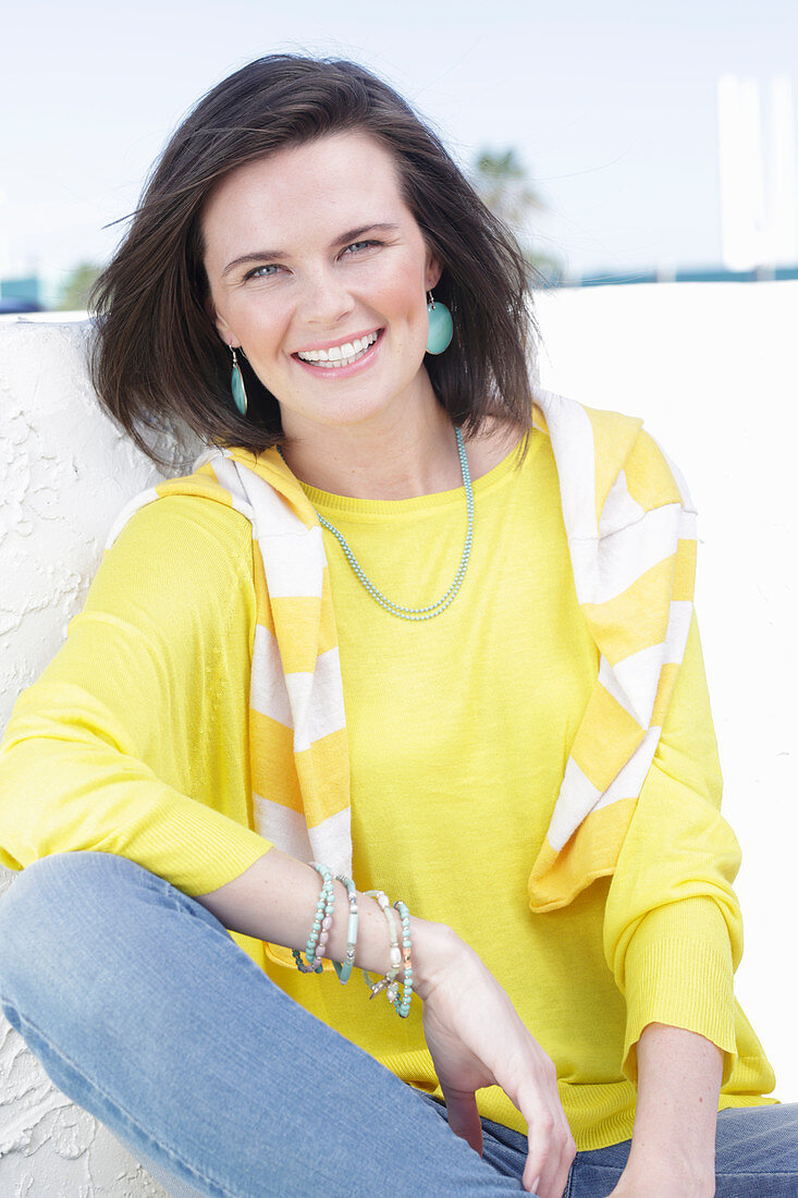 A young woman wearing a long-sleeved yellow top and jeans with a jumper over her shoulders