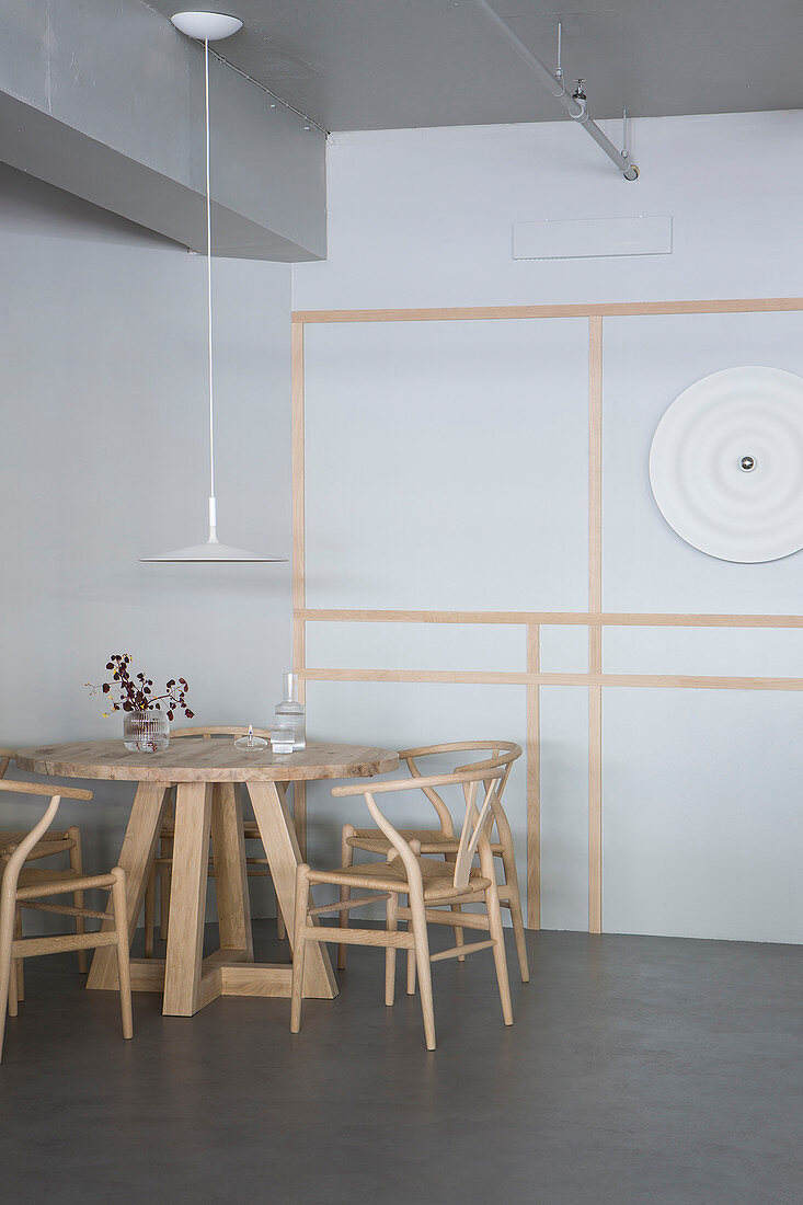 Designer chairs at round wooden table against grey walls with decorative trim