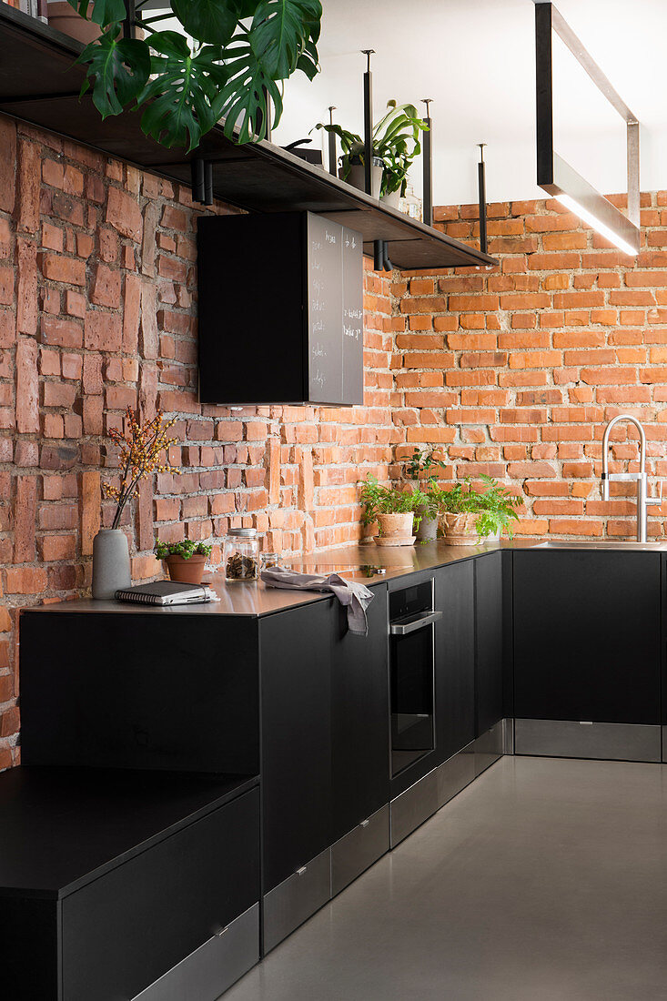 Schwarze Küche mit Schubladen in der Sockelleiste und Backsteinwand