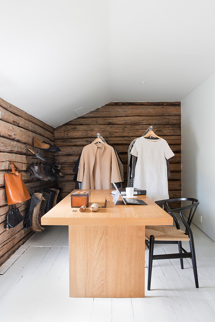 Modern desk in room with rustic wooden walls and clothes rails