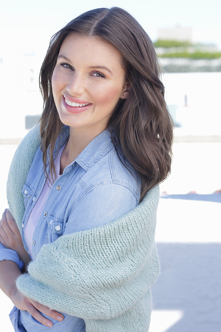 A young woman wearing a denim shirt with a jumper over her shoulders