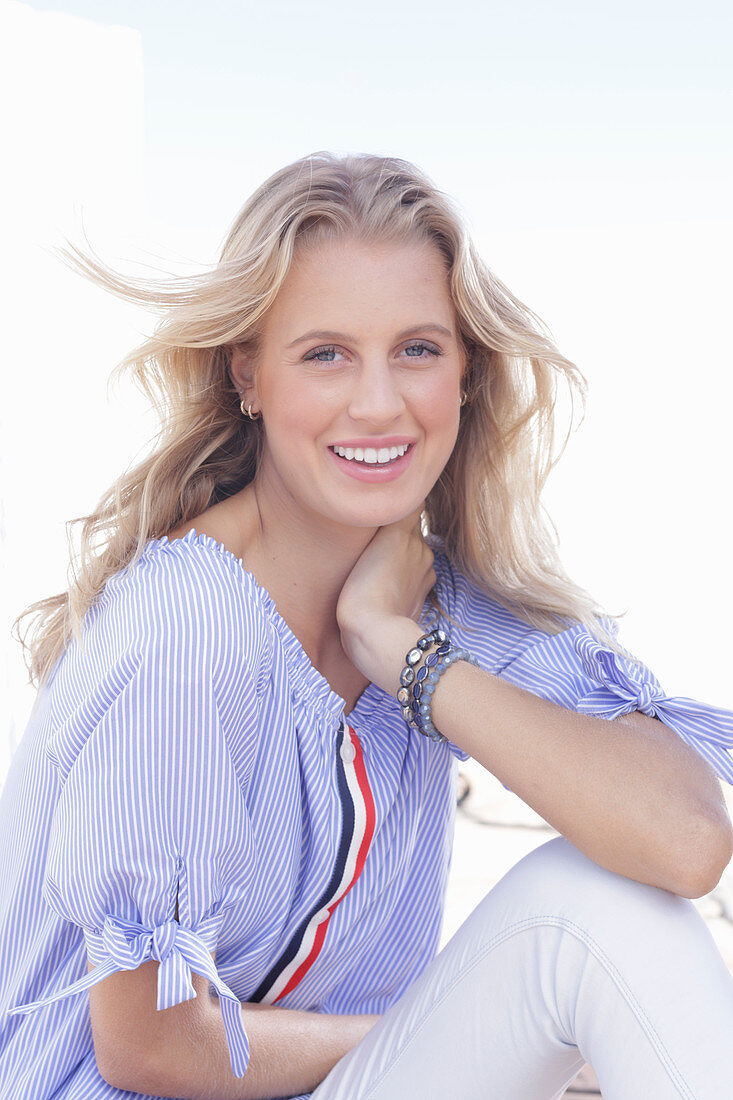 A young blonde woman wearing a blue-and-white striped Carmen blouse and white trousers