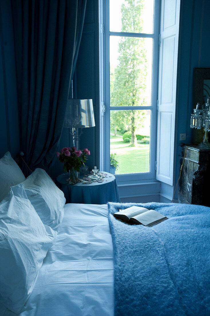 Bed and bedside table next to window in blue bedroom