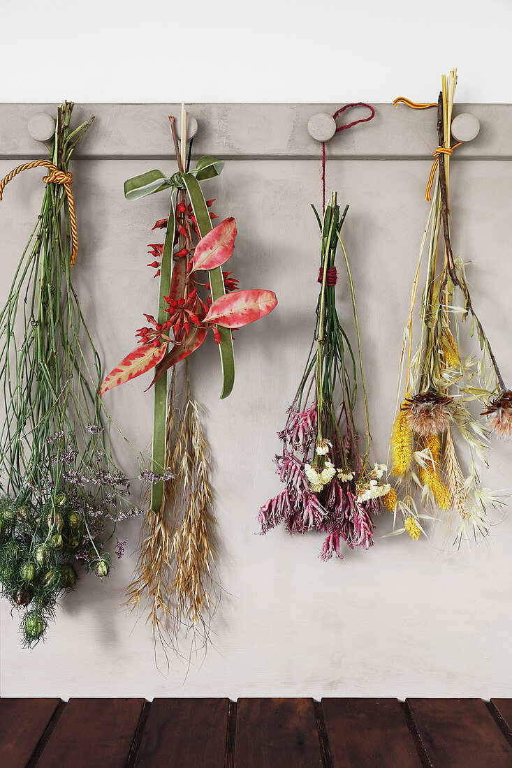 Sträuße mit getrockneten Blumen und Gräsern an einer Hakenleiste