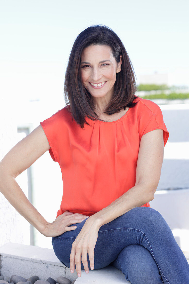 Reife, brünette Frau in roter Bluse und Jeans