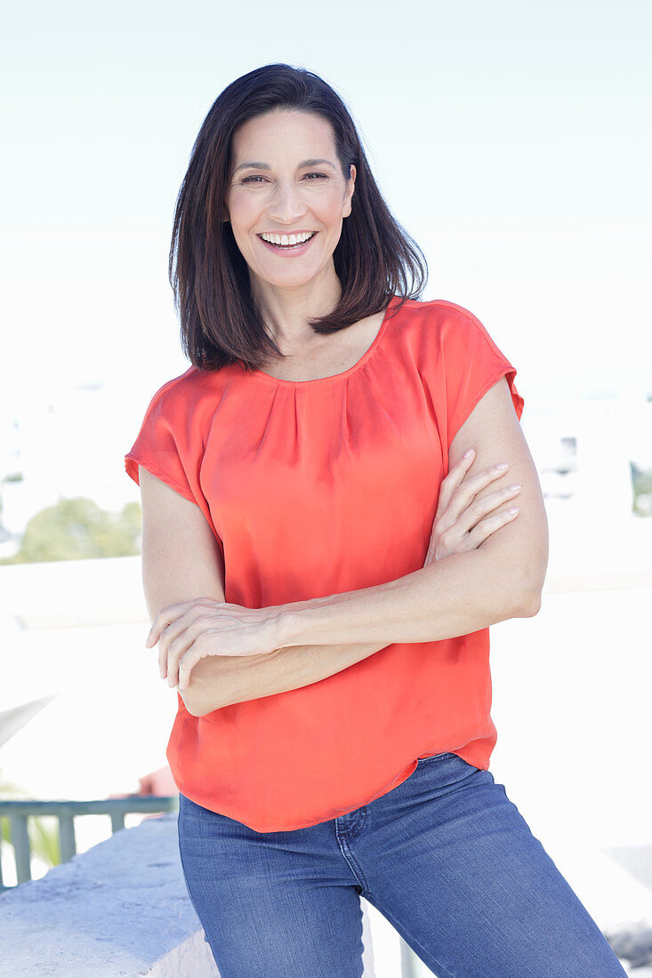 Reife, brünette Frau in roter Bluse und Jeans