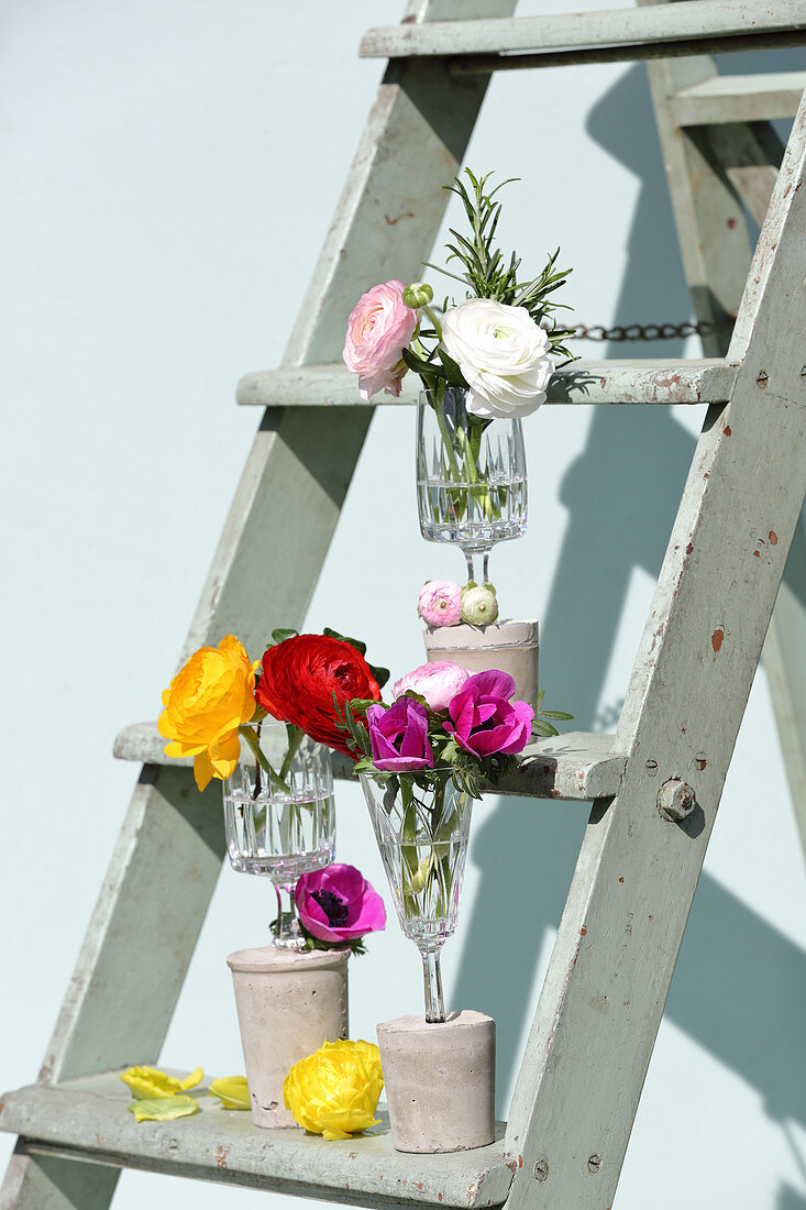 Flowers in vases made from wine glasses with concrete bases on stepladder