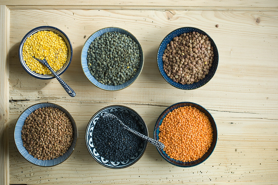 Various types of lentils in small bowls on a rustic wooden table