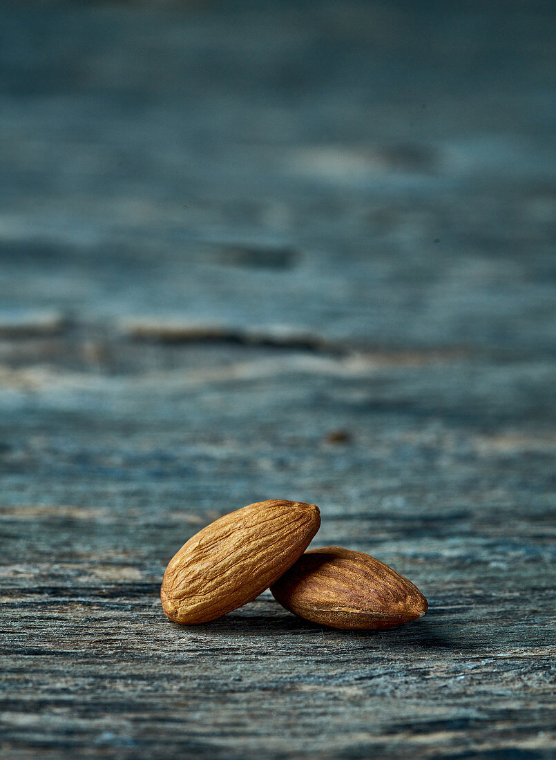 Two shelled almonds on a wooden surface