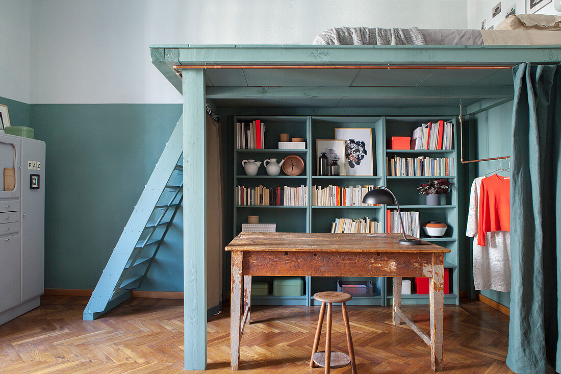 Shelves, wooden table and clothes rail below DIY loft bed