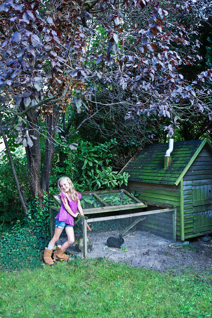 Little girl next to rabbit run in garden