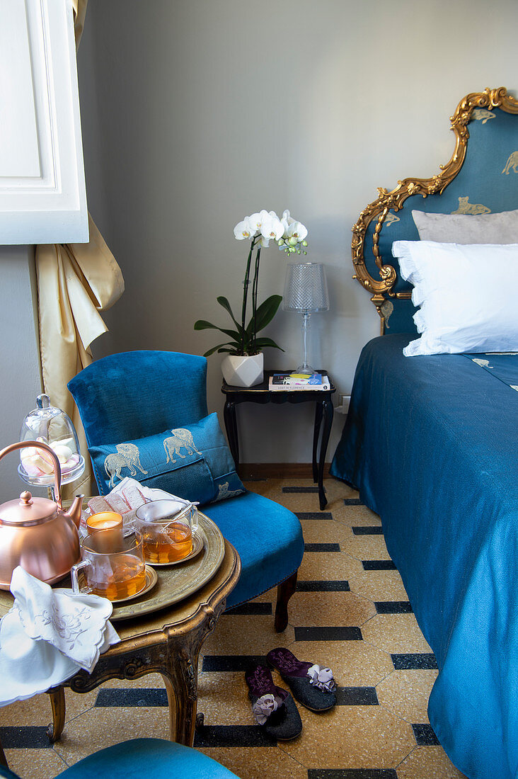 Tea and cake on a side table next to a opulent blue bed with carved golden frames