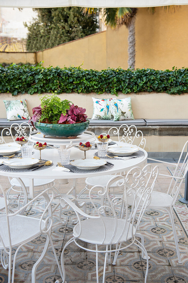 Set table on terrace table with ornate, white metal chairs