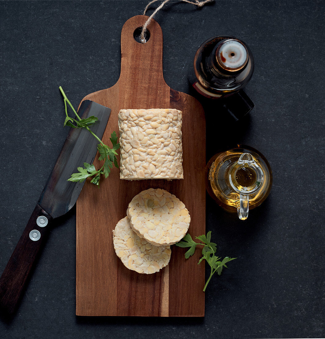 A roll of tempeh and a slices on a wooden board