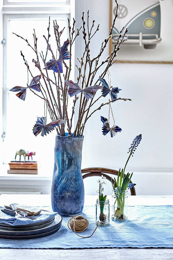 Aus Papier gefaltete Schmetterlinge an Weidenzweigen in blauer Vase