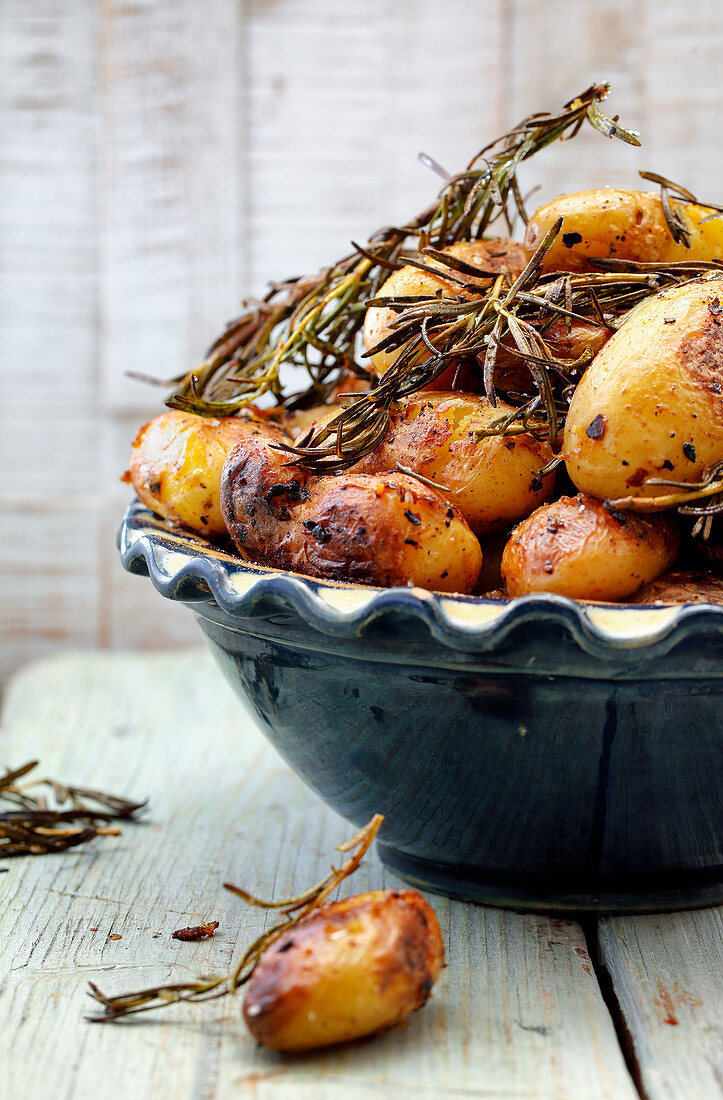 Roasted potatoes with sprigs of rosemary in a ceramic bowl