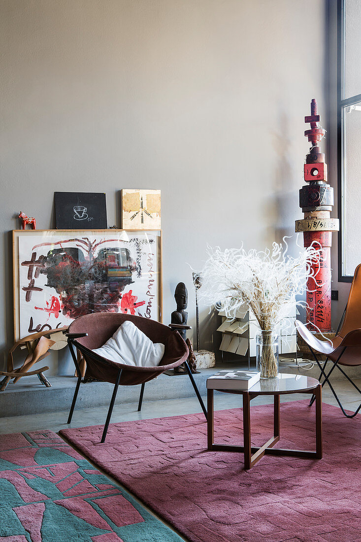 Side table and easy chairs on pink rug in front of various artworks