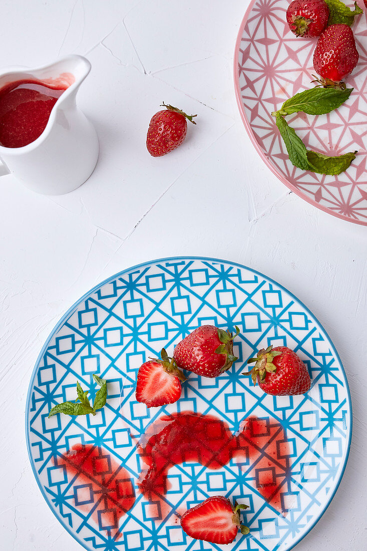 Ein Kännchen Erdbeersauce daneben frische Erdbeeren und Saucenrest auf Teller