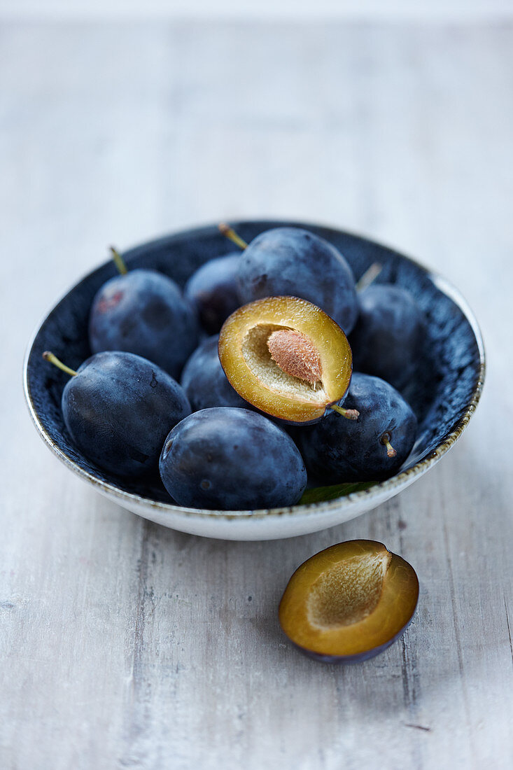 Fresh plums in a bowl on a light background