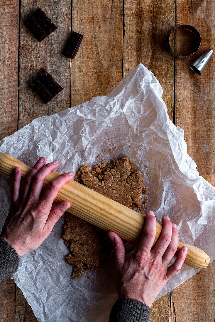 Person rolling chocolate dough with rolling pin on white baking paper