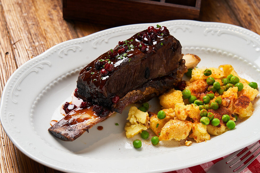 Roasted steak on bone with berry sauce and baked potatoes with young green peas on white plate