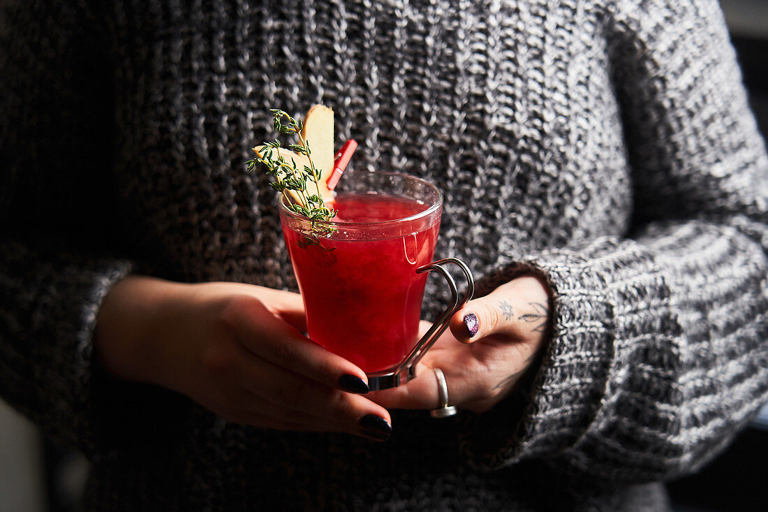 Woman in holding glass with red punch decorated with rosemary and slices of ginger