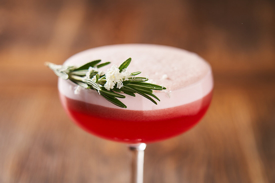 Glass with red cocktail consist of gin egg whites lime juice and raspberry syrup decorated with rosemary