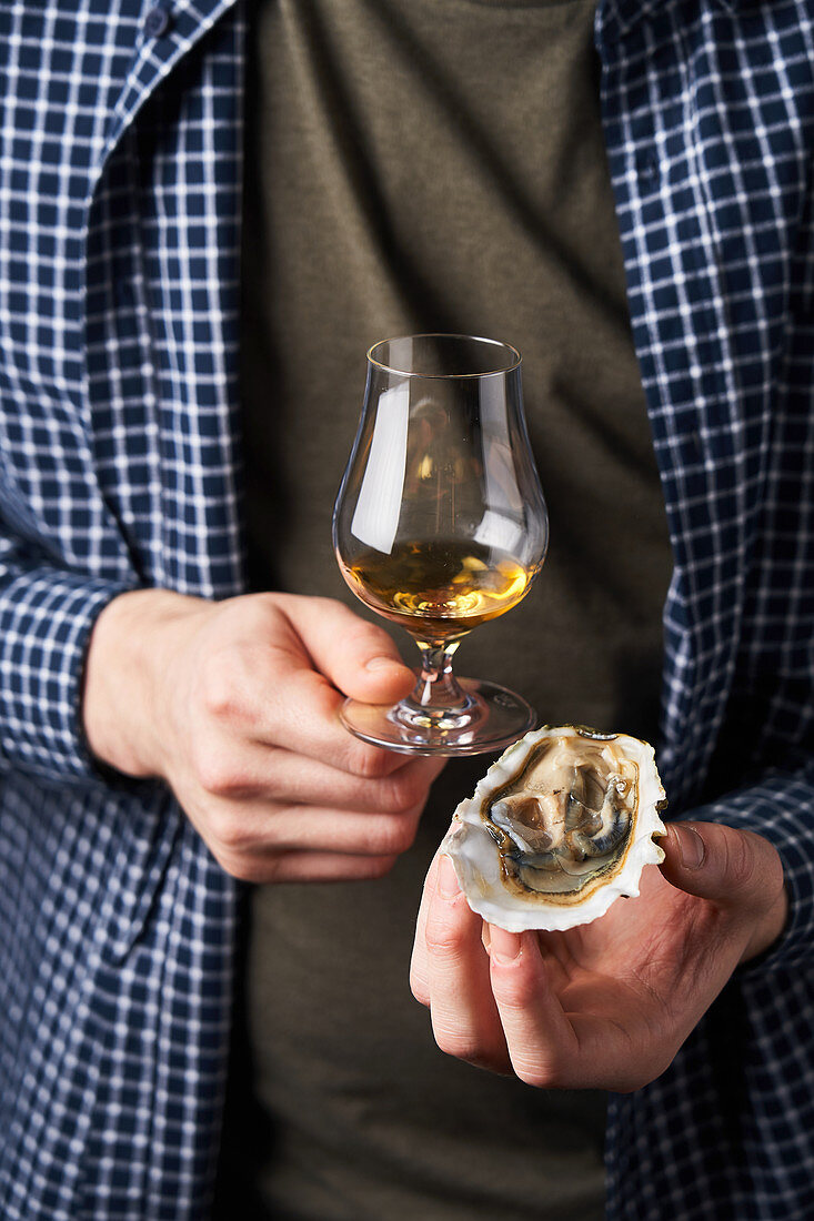 Guy with modern glass of whiskey and delicious clam in hands