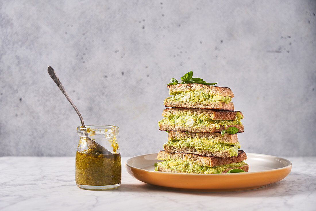 Rye bread sandwiches with avocado puree with glass jar of pesto sauce