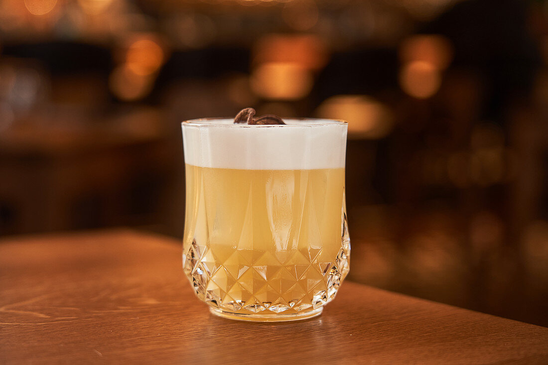 Glass of classic Whiskey Sour with lemon juice and egg white placed on wooden counter