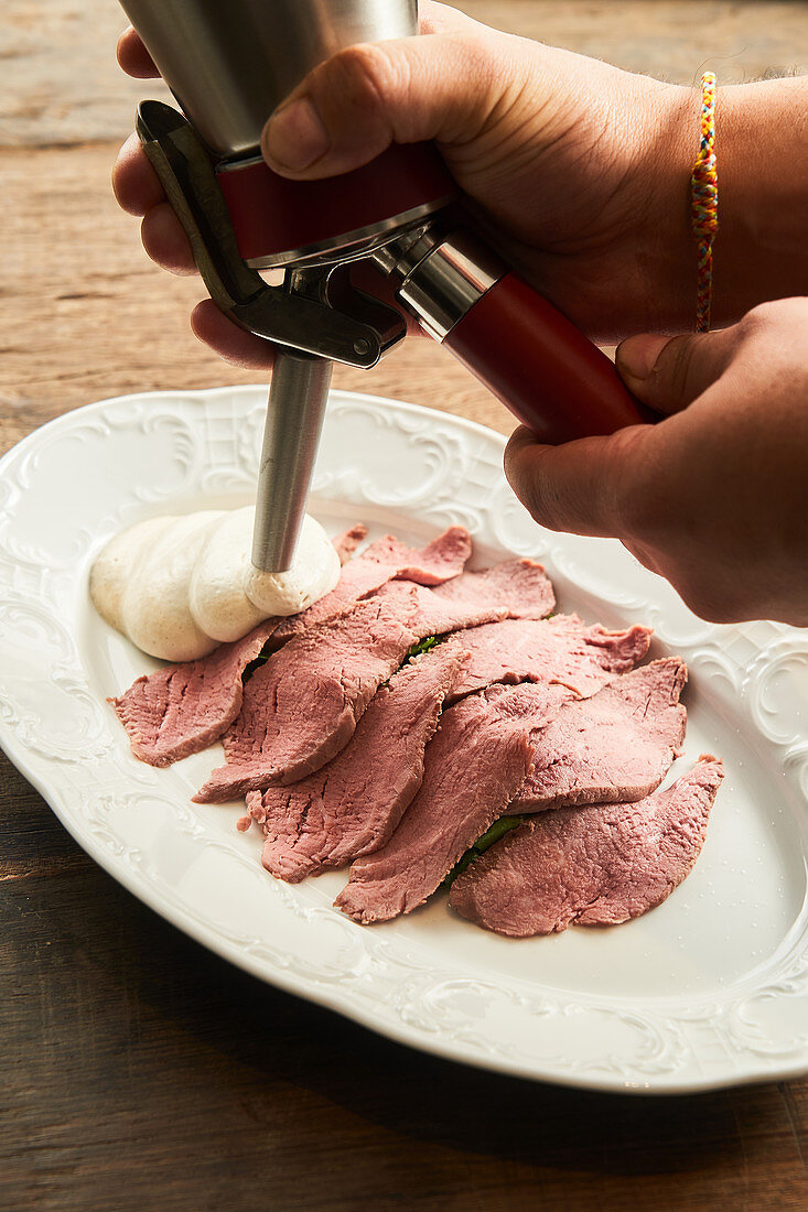 Chef adding fluffy sauce on plate with slices of gentle roast beef meat