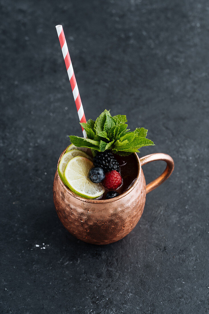 Metal mug with fruit drink with lime and berries decorated with mint leaves