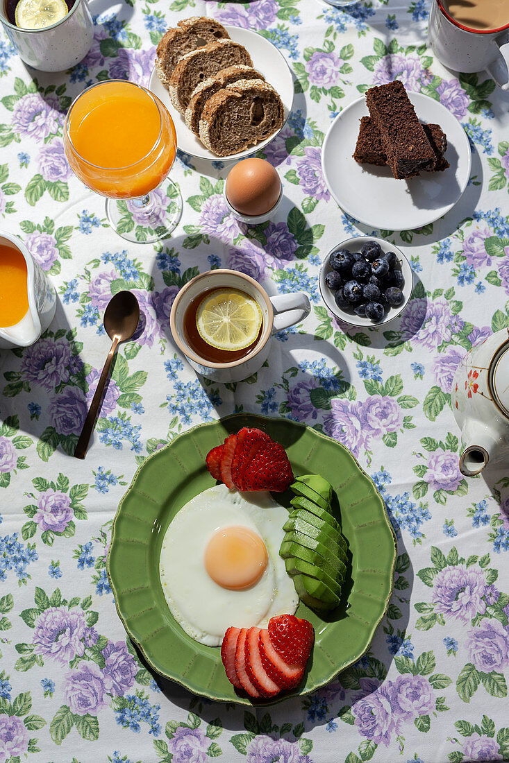 Breakfast with eggs, avocado, berries, cake, toast, tea and orange juice