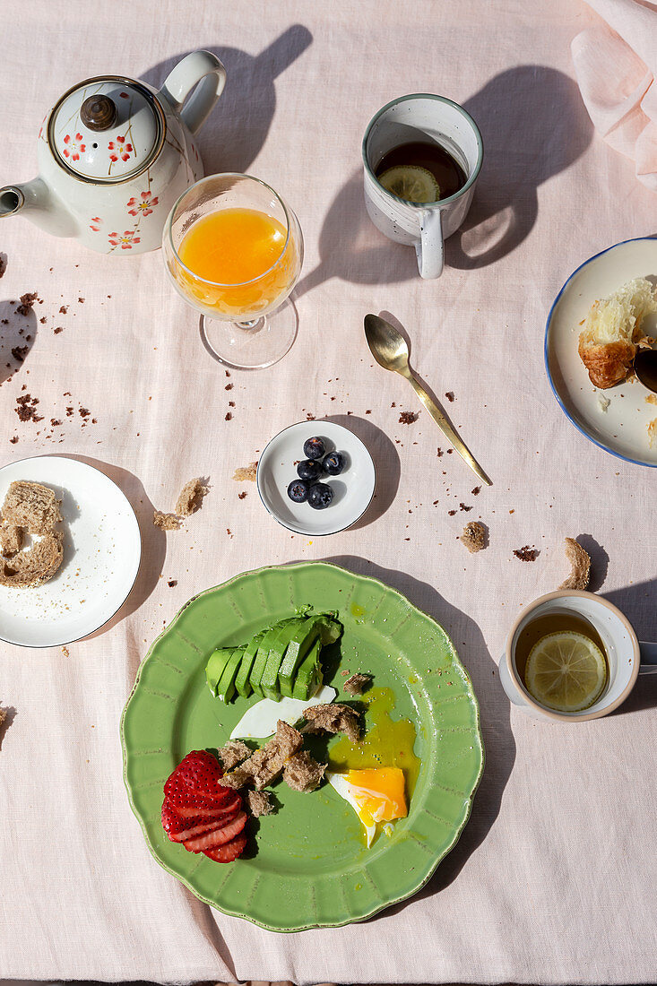 Reste eines Frühstücks mit Ei, Obst, Avocado, Croissants, Brot, Orangensaft und Schwarztee