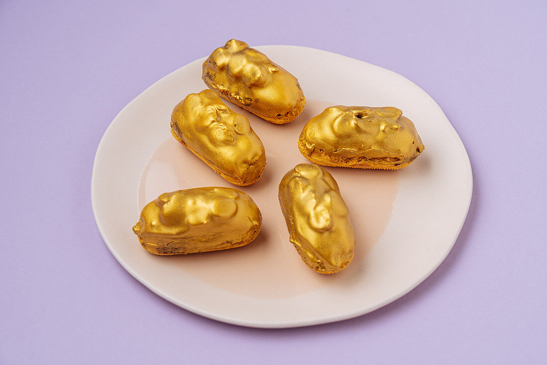 Eclairs with golden icing placed on plate on lilac background