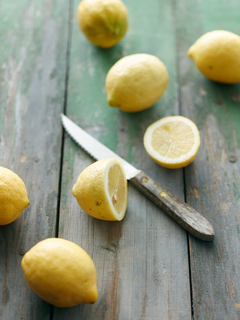 Zitronen, ganz und halbiert mit Messer auf Holzuntergrund