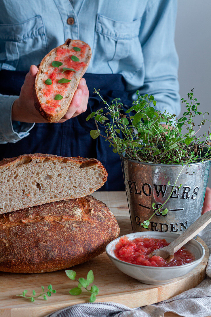 Female spreading with spoon red sauce on sourdough bread on wooden table with green plant