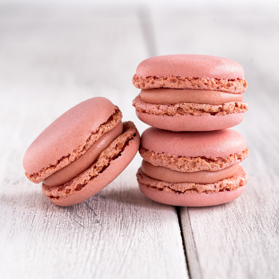 Pink macaroons stacked in pile against wooden white surface
