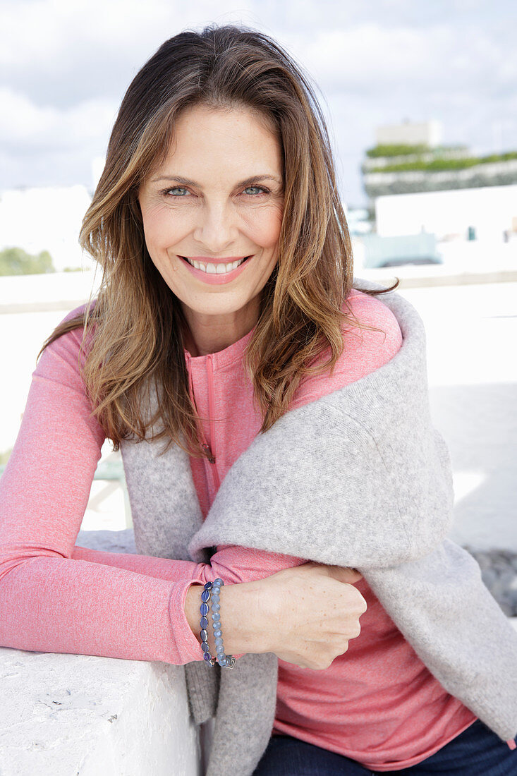 A long-haired woman wearing a pink top with a grey jumper over her shoulders