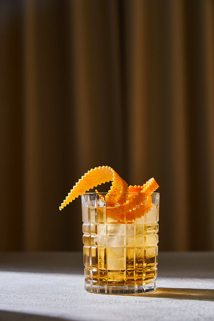 Glass cup with cold old fashioned cocktail with whiskey and orange peel