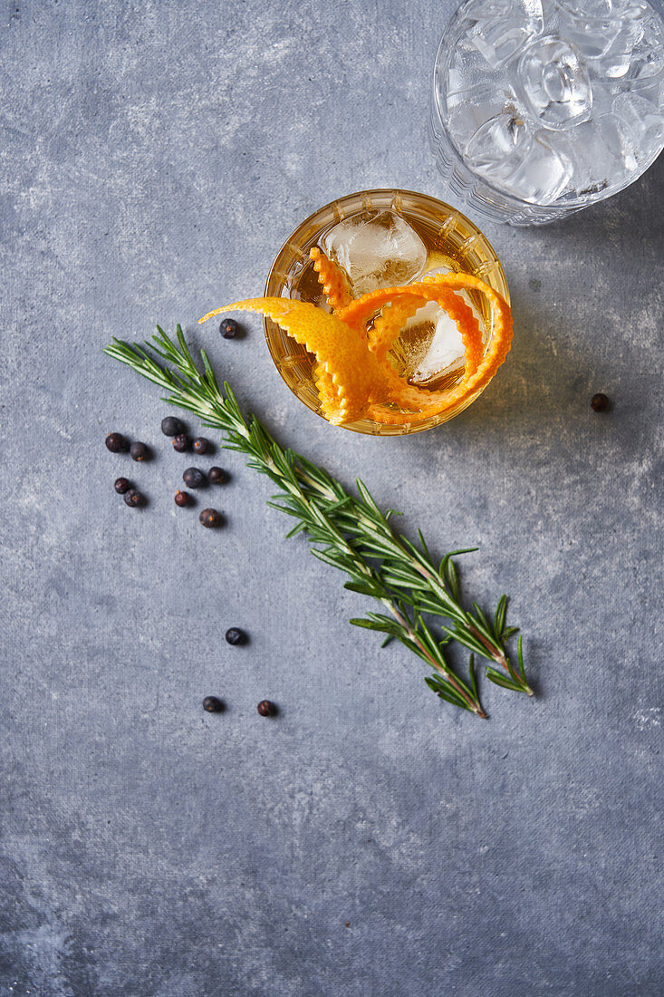 Old fashioned cocktail with whiskey and orange peel with rosemary plant, pepper grains