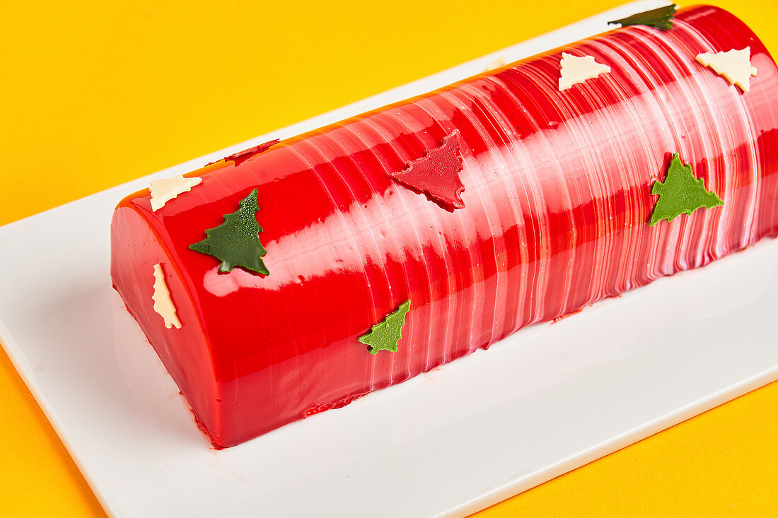 Cake with red icing and Christmas trees placed on board on yellow background