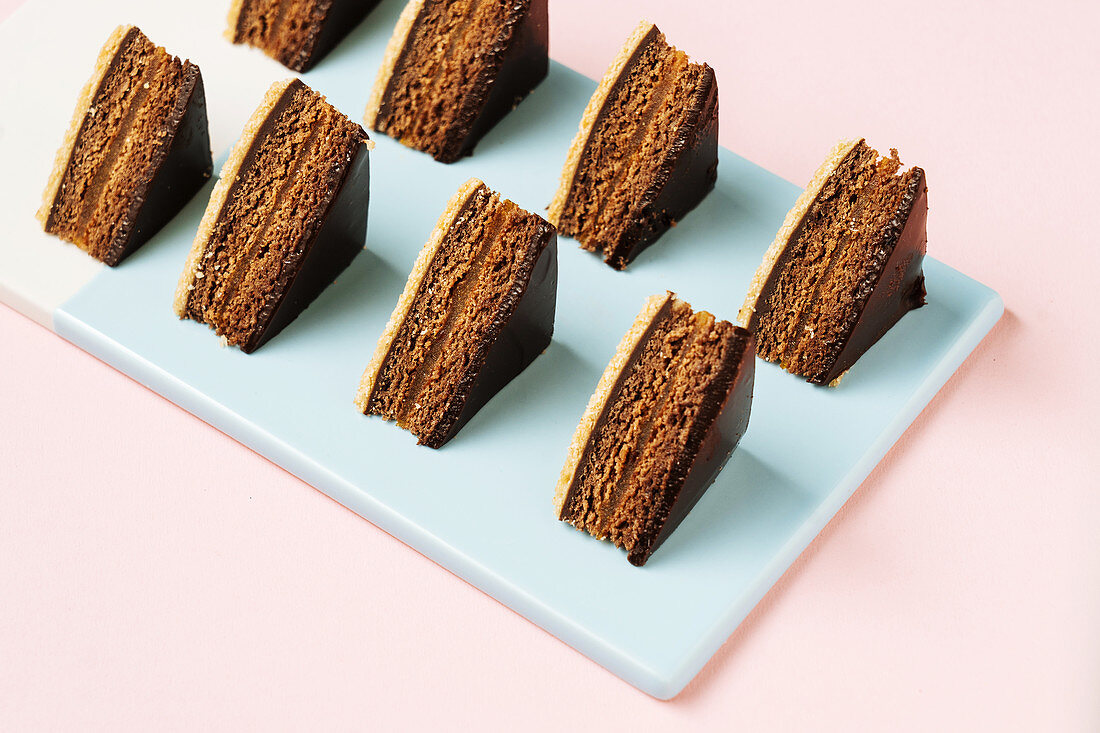 Pieces of chocolate cake placed in rows on blue board on pink background